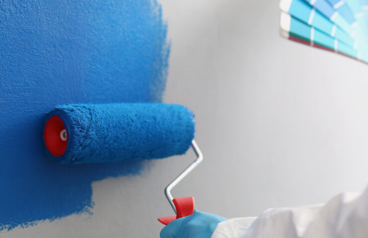 Painter with brush tool covered in blue colour painting wall, worker on site